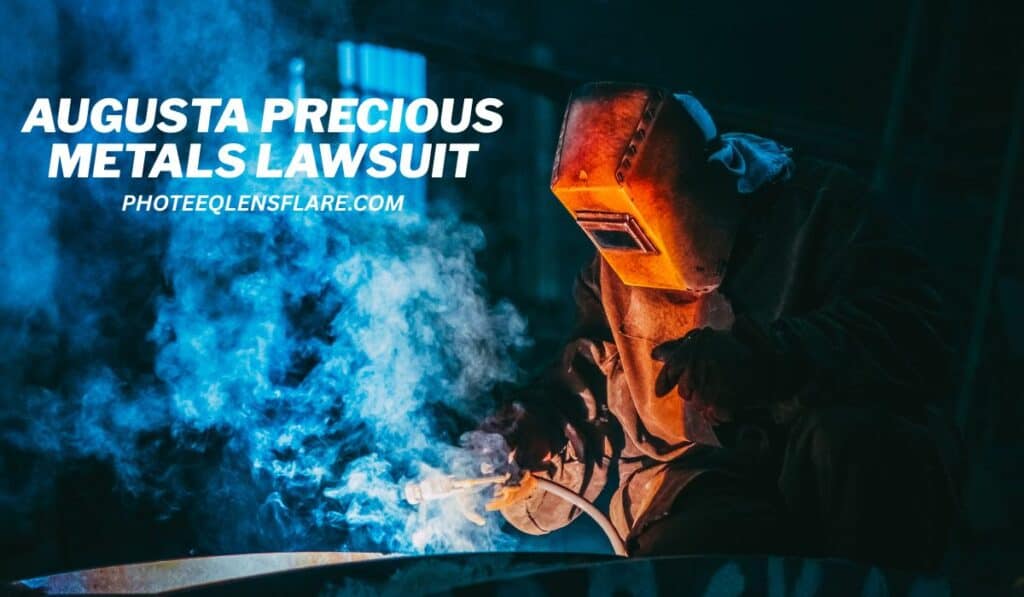A welder in protective gear works with intense sparks and smoke in an industrial setting. The image has a bright orange glow from the welding torch and a dark, moody background. Text overlays the image, reading "AUGUSTA PRECIOUS METALS LAWSUIT" and the website "PHOTEEQLENSFLARE.COM."