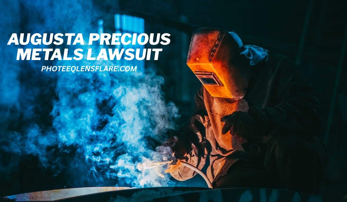A welder in protective gear works with intense sparks and smoke in an industrial setting. The image has a bright orange glow from the welding torch and a dark, moody background. Text overlays the image, reading "AUGUSTA PRECIOUS METALS LAWSUIT" and the website "PHOTEEQLENSFLARE.COM."